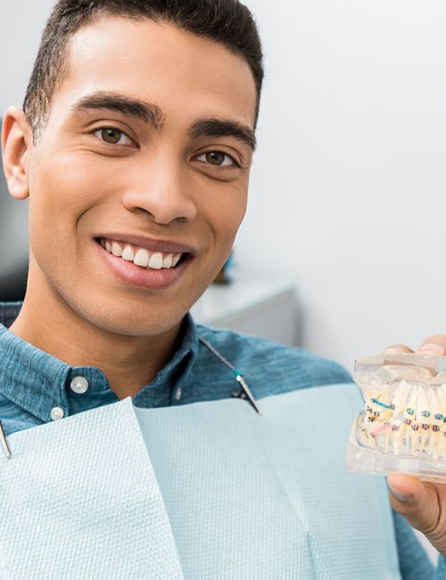 handsome african american man holding dental jaw model with braces